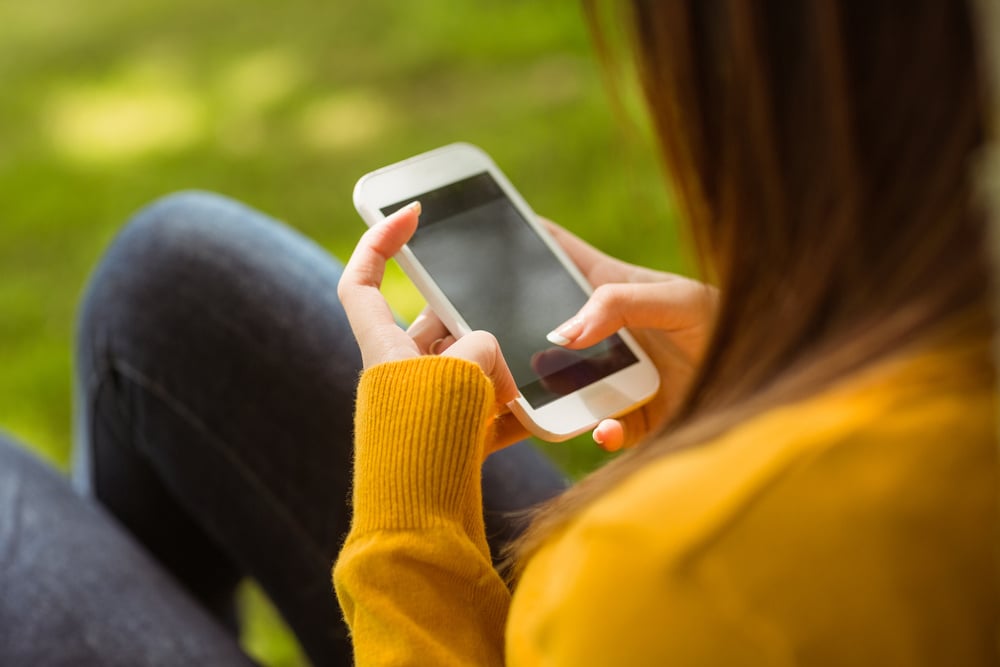 Side view of young woman text messaging in the park Side view of young woman text messaging in the park